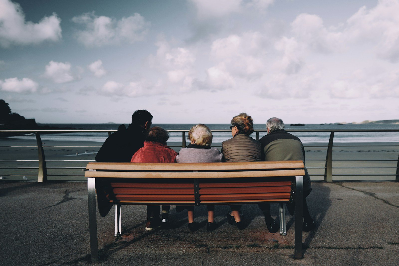 Group of older friends sitting on a bench looking out at the sea