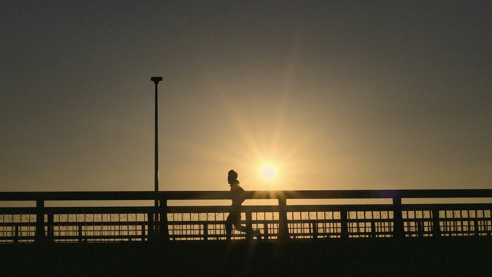 Silhouette of a person running on a bridge at sunrise