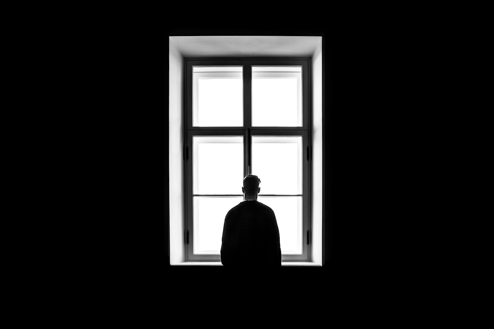 Silhouette of a person seen from behind standing alone at a bright window