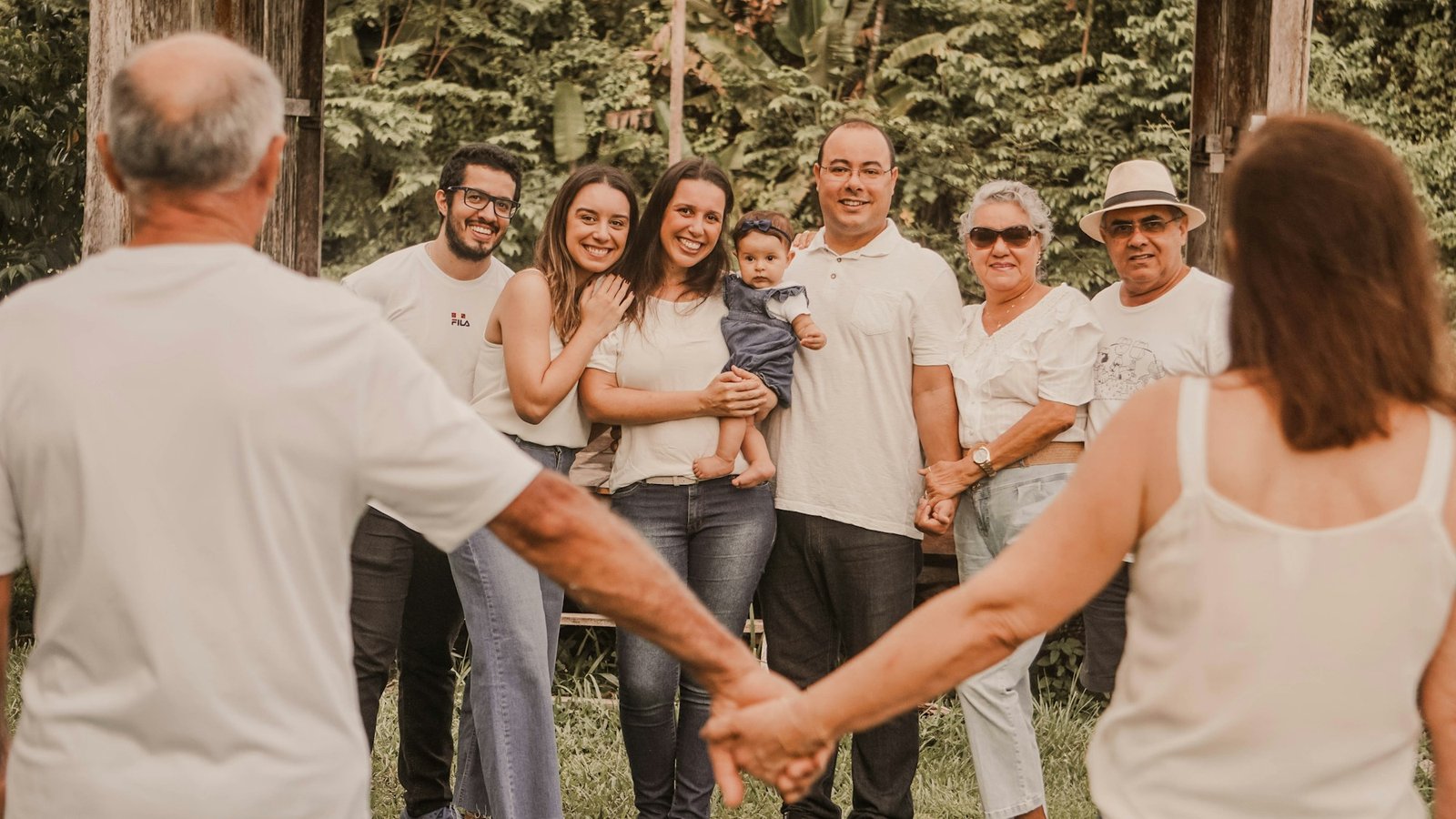 Three generations of a family smiling and holding hands outdoors