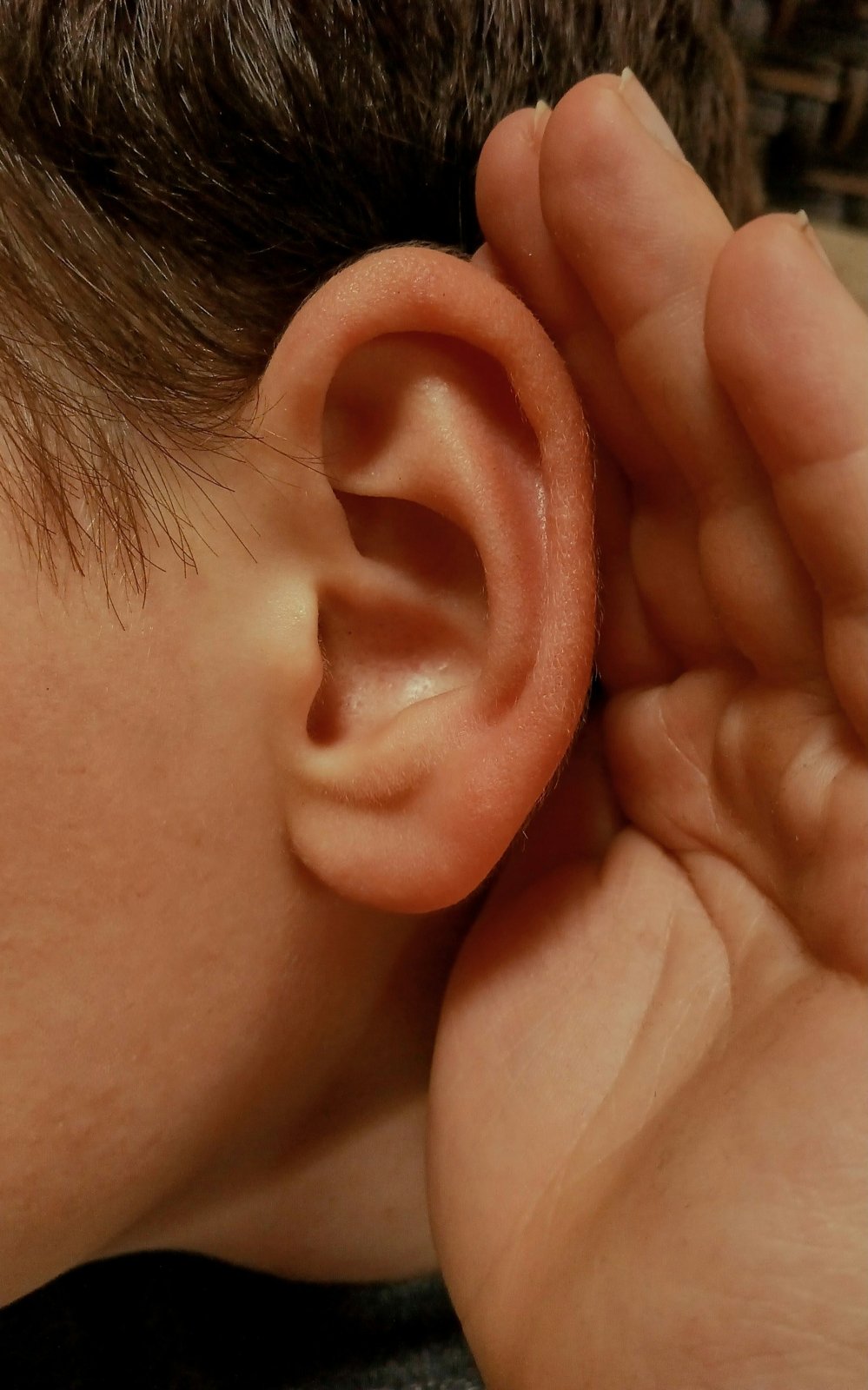 A hand cupped behind an ear to listen closely
