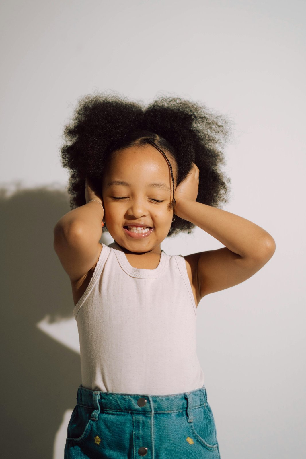 Smiling girl with eyes closed covering her ears with both palms