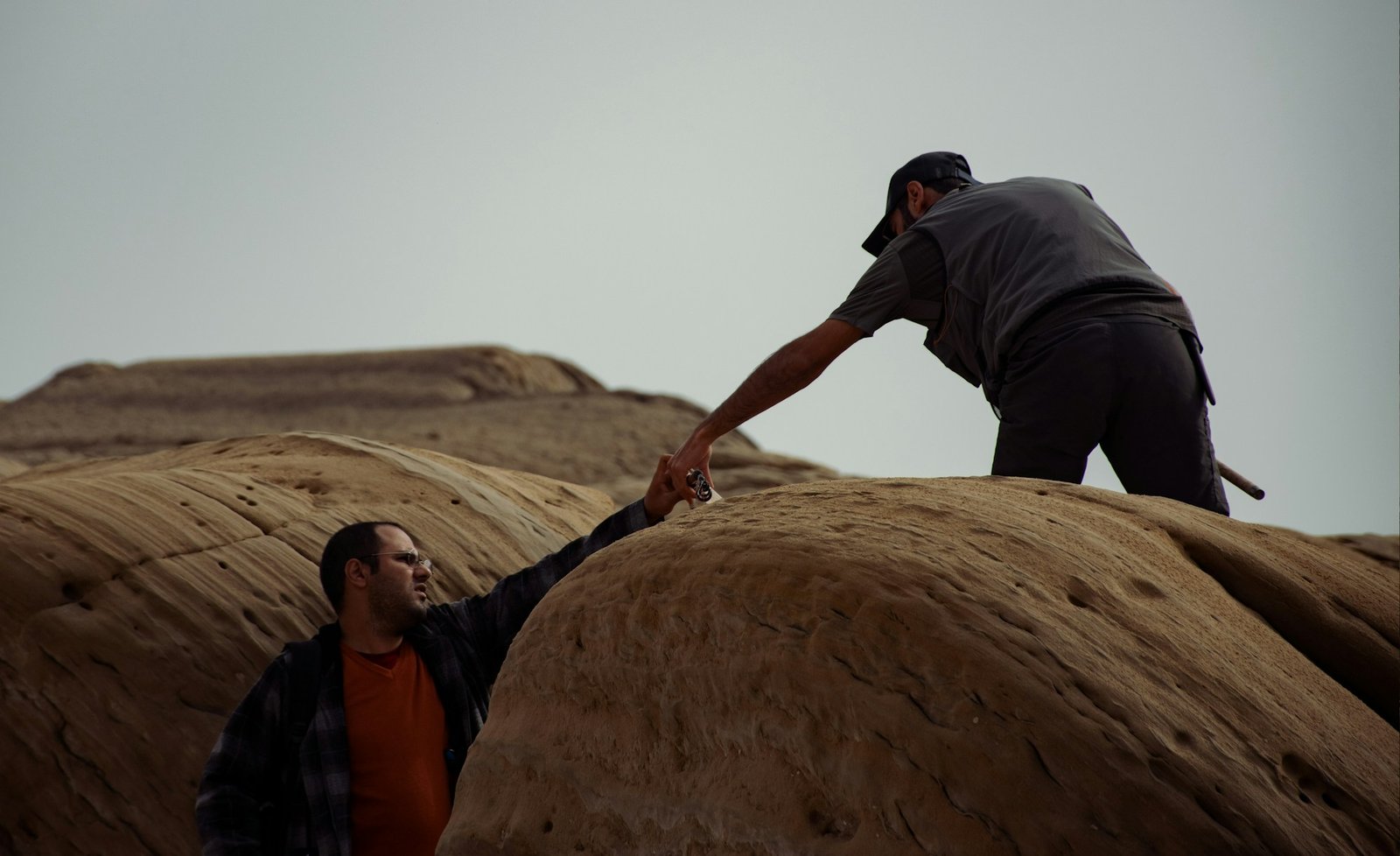 A man reaching down to help another climb up a rock