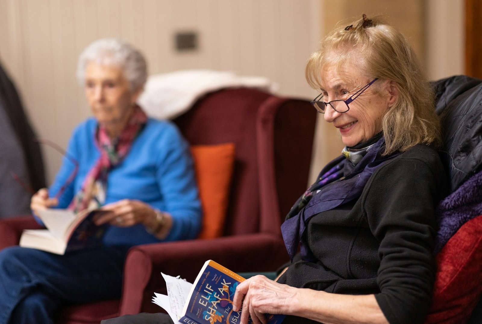 Two older women chatting in armchairs, books in hand