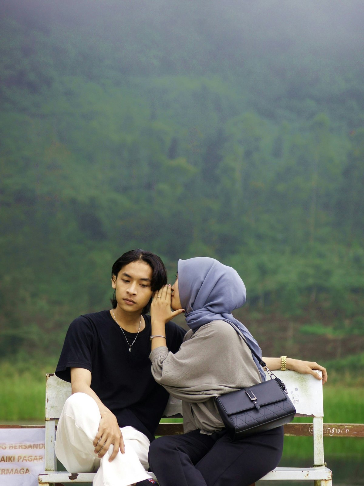 Young woman whispering into a young man's ear on a bench