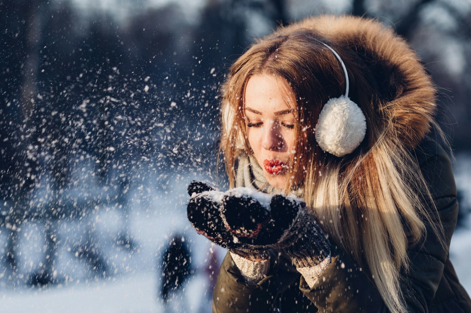 Woman wearing earmuffs blowing snow off her gloves