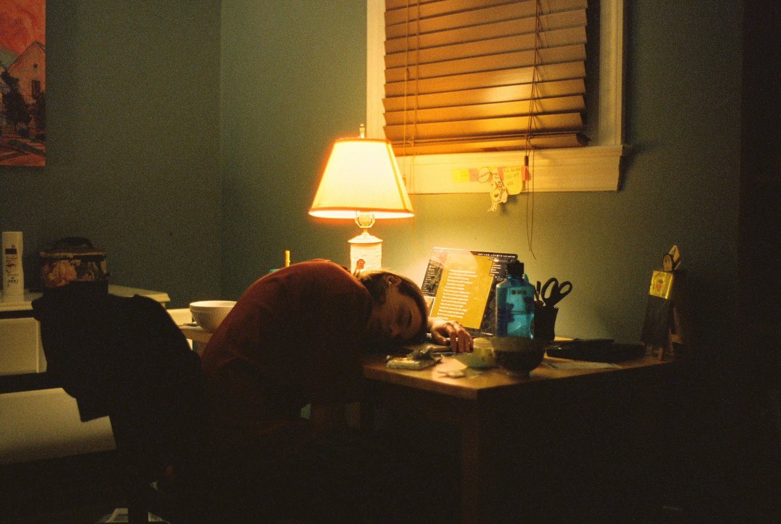 Person asleep at a desk under a lamp late at night