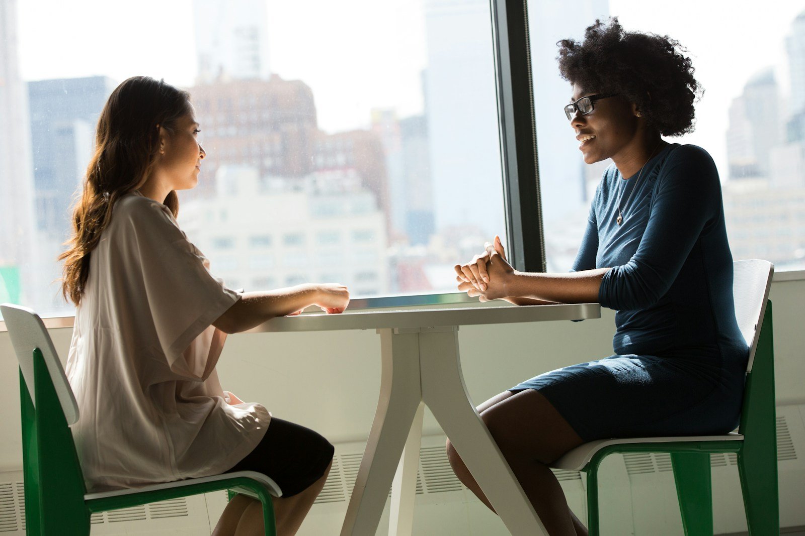 Two people talking across a table by a large window