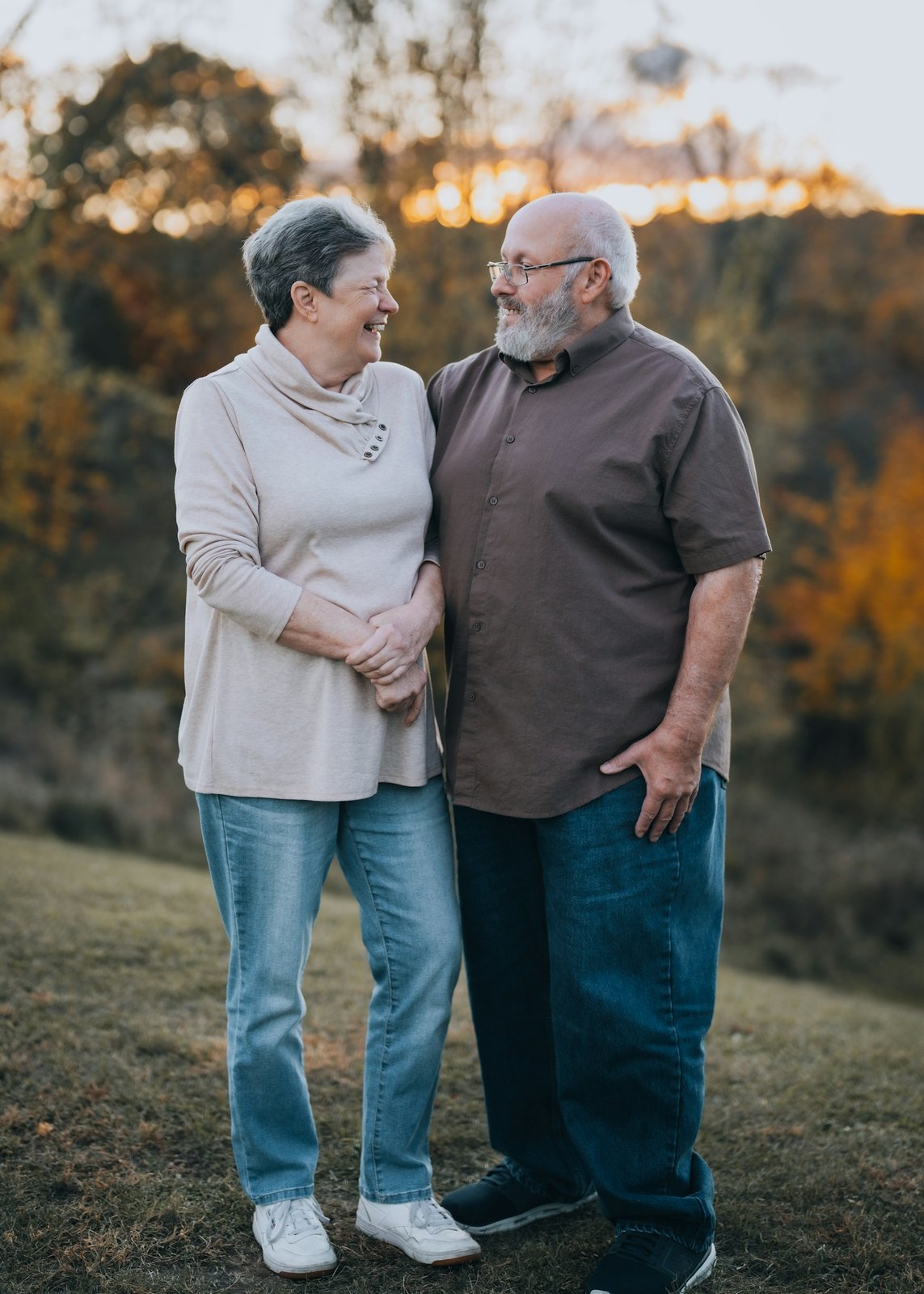 Older couple standing side by side in a field, smiling at each other