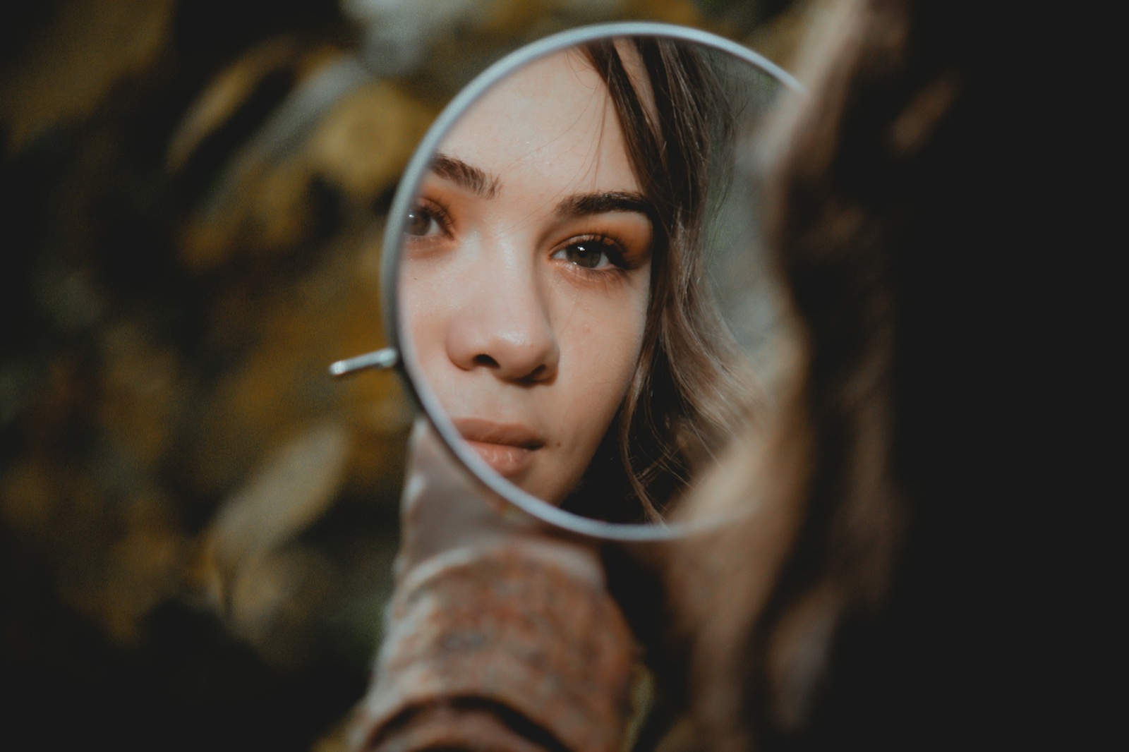 Woman looking at her face in a small round hand mirror