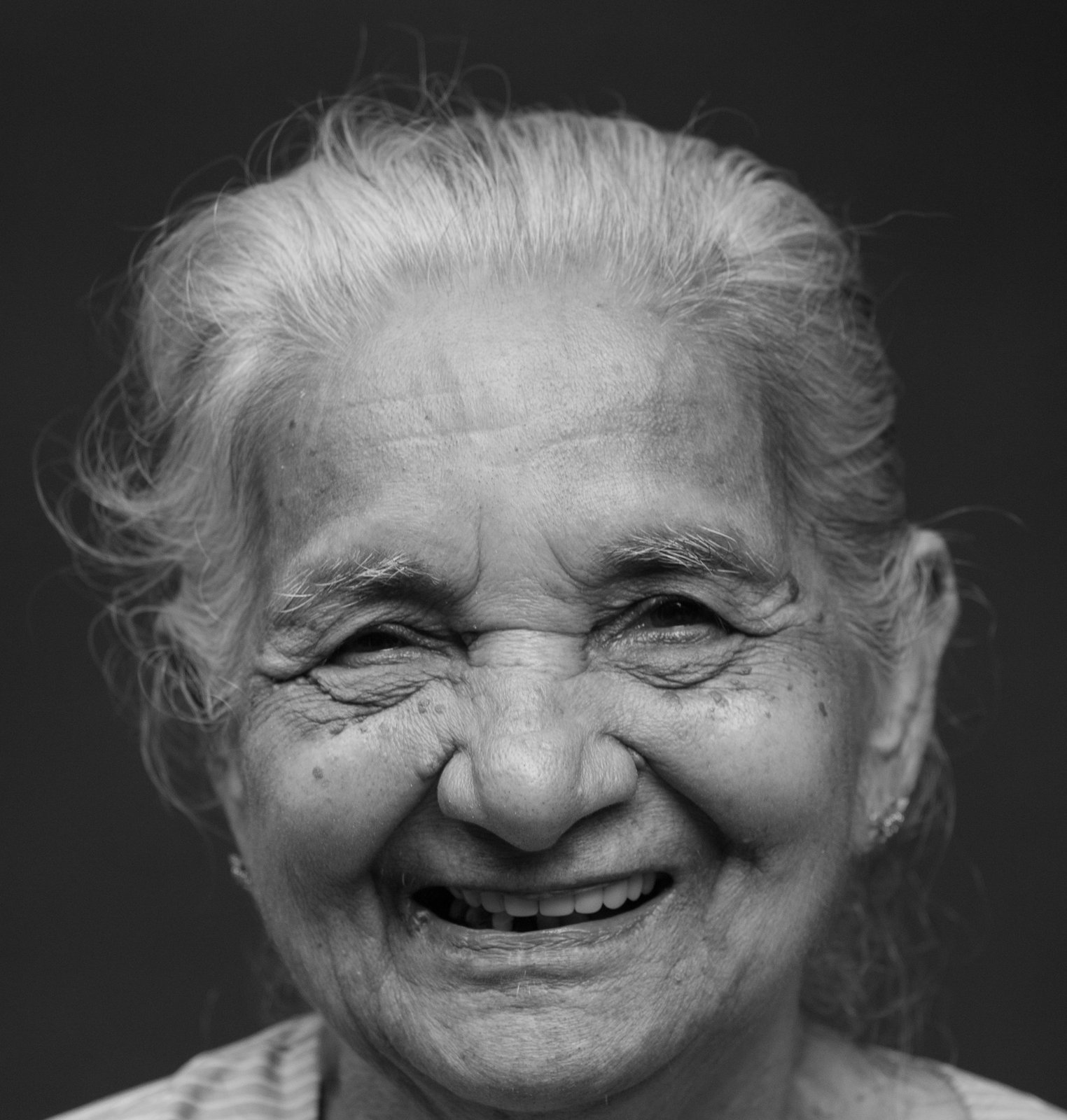 Elderly woman smiling broadly, with upturned wrinkles at the corners of her mouth