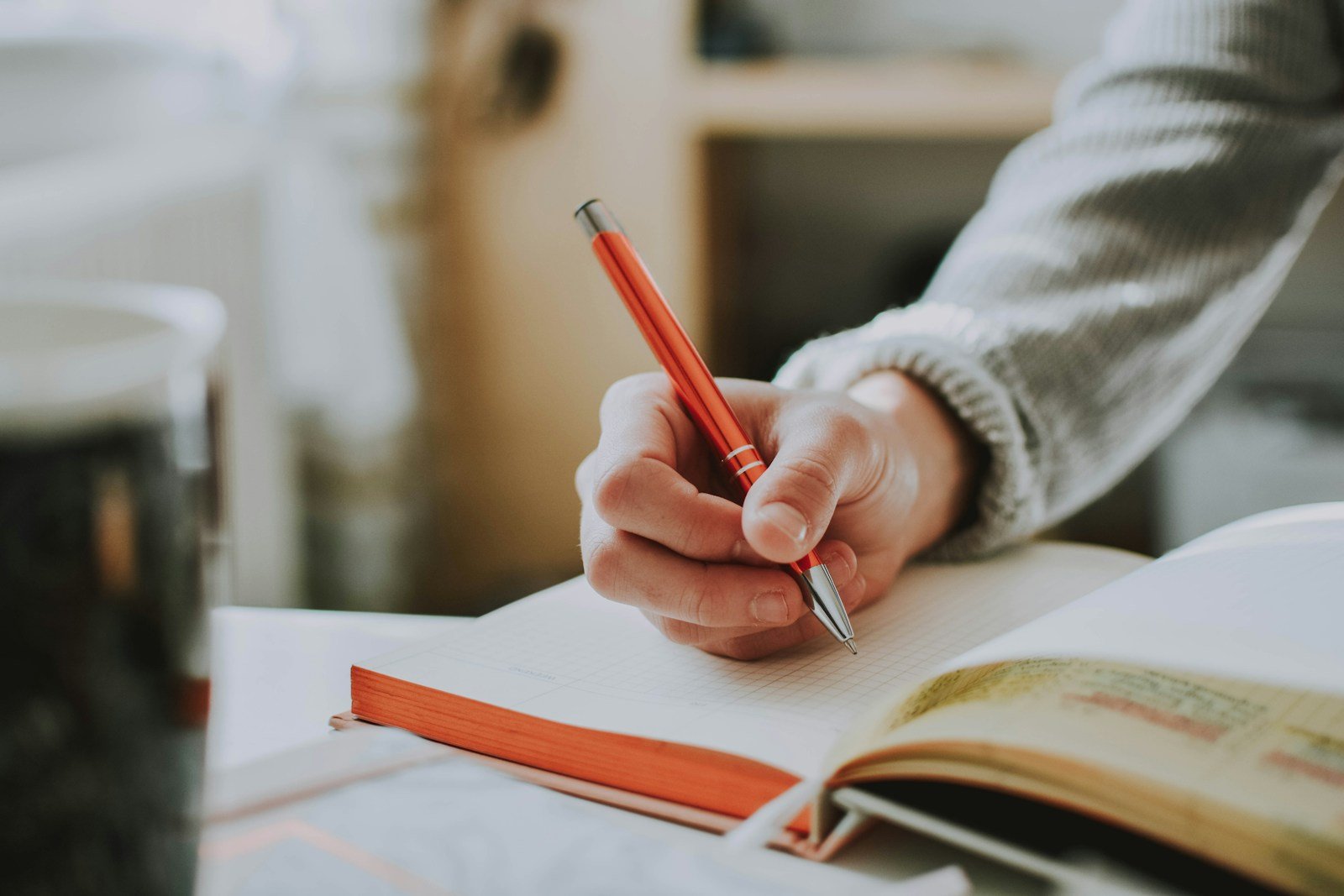 Hand writing notes with a red pen in an open notebook
