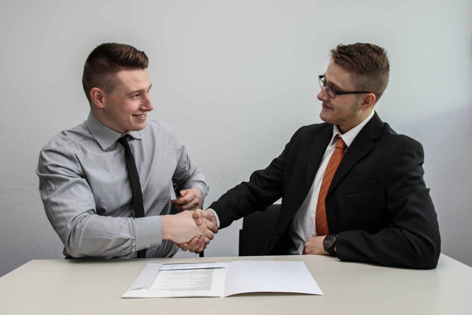 Two men shaking hands and smiling across a meeting table