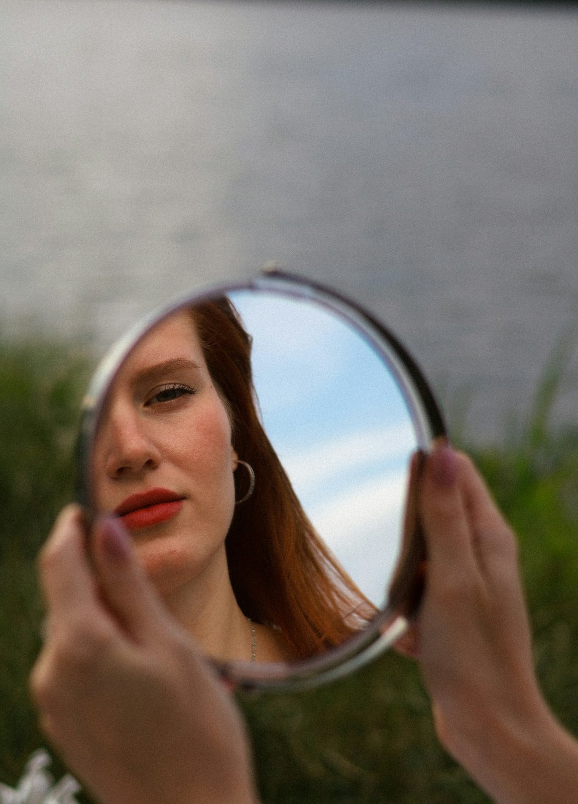 Woman holding up a small round mirror and looking at her reflection