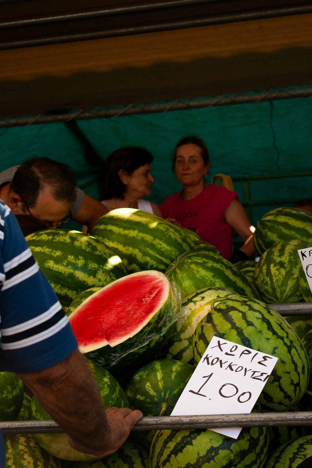 Market stall piled high with watermelons and a handwritten price sign