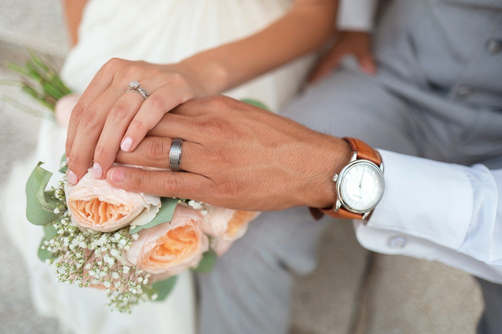Couple's hands with wedding rings resting on a bouquet